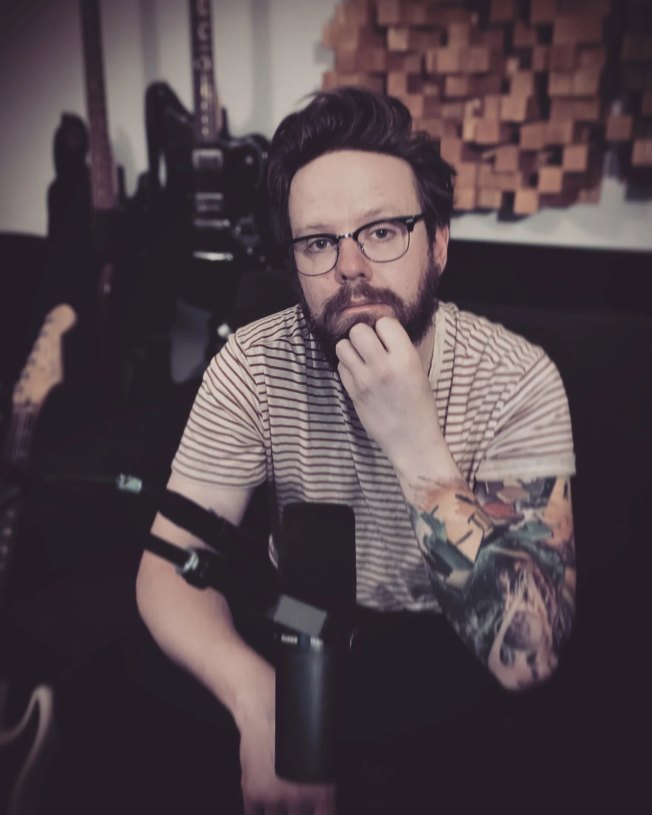 Robb Jolley seated with a microphone and guitars in his studio